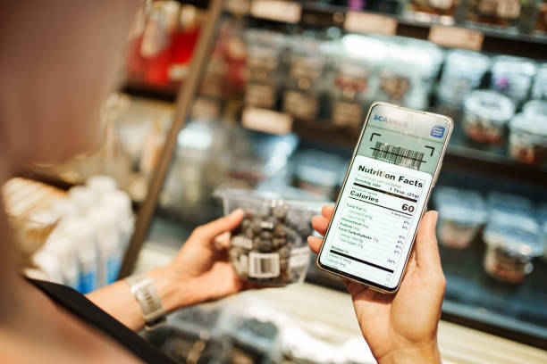 Gros plan d’une femme scannant le code-barres du produit et lisant les détails nutritionnels sur le smartphone